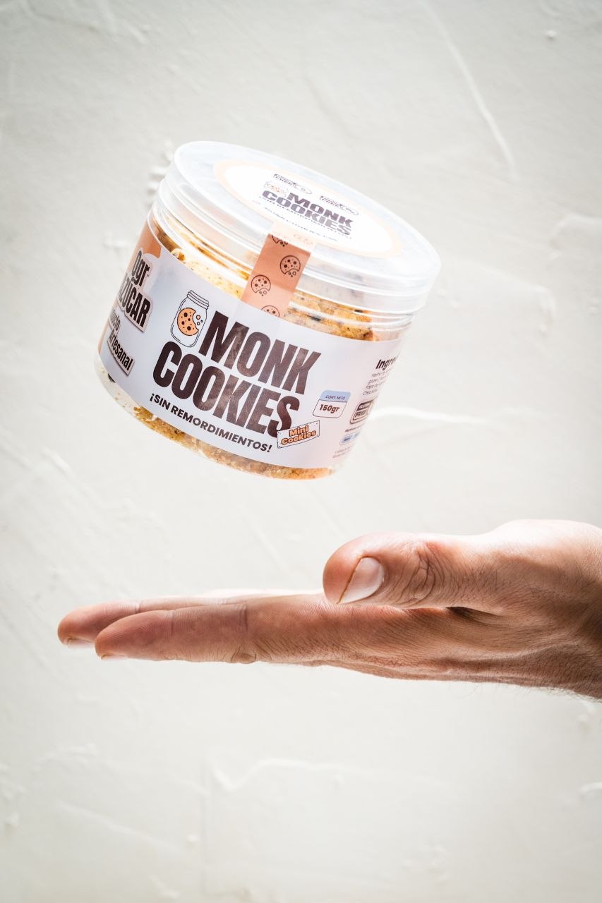 Pote de Monk Cookies cayendo en el aire sobre una mano